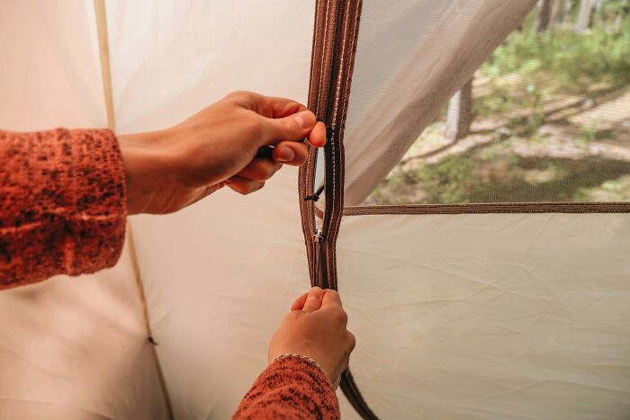 Hands nervously unzipping a tent zipper revealing a blurred forest, capturing terrifying real-life moments outdoors.