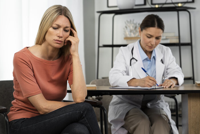 Worried woman consulting with a medical professional in white coat taking notes during a tense health discussion.