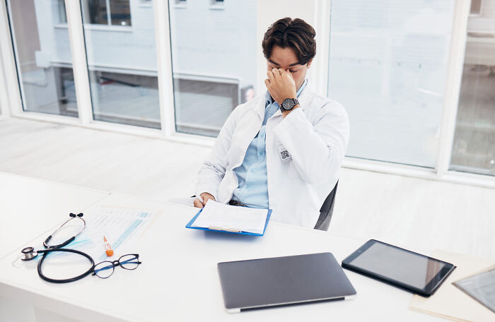 Medical professional in white coat looking frustrated at desk with stethoscope and tablet, reflecting on anti-vaxxer encounter.
