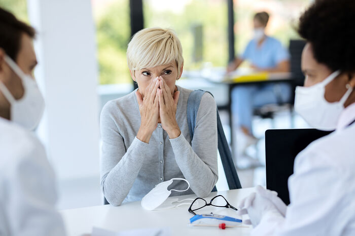 Medical professionals wearing masks listening to a concerned woman in a clinical setting during an anti-vaxxer discussion.