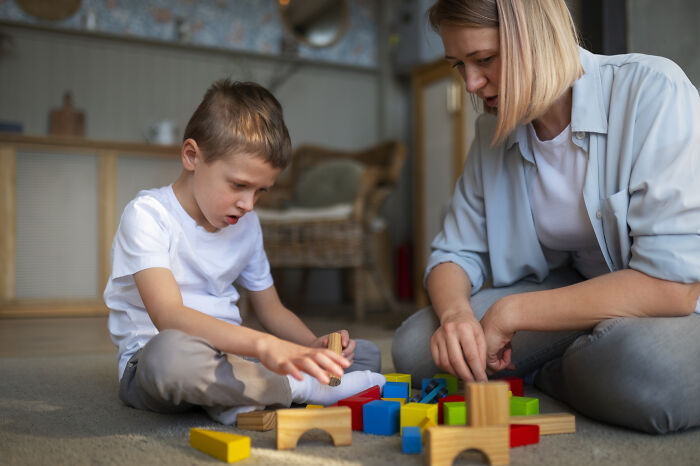 Medical professional engaging thoughtfully with a child playing with colorful building blocks in a cozy indoor setting.