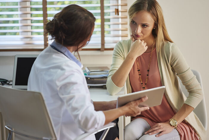 Medical professional consulting a young woman, discussing vaccine concerns in a bright office setting with a tablet.