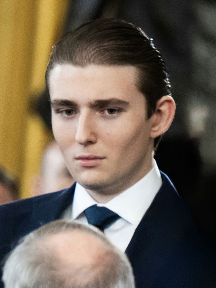 Barron Trump em um terno formal, parecendo sério durante um evento relacionado a um incidente de chamada de emergência.