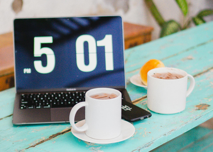 Laptop showing 5:01 PM with two coffee mugs on a rustic table highlighting Dutch worker logging off at 5PM concept. Laptop showing 5:01 PM with two coffee mugs on a rustic table highlighting Dutch worker logging off at 5PM concept.