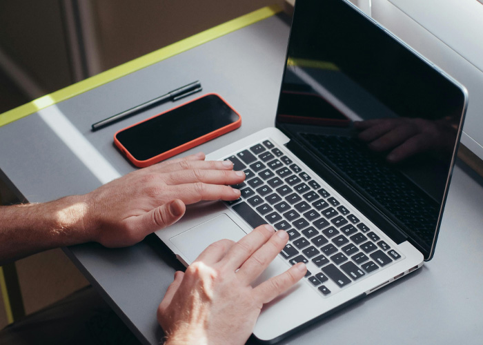 Dutch worker typing on laptop at desk with phone nearby, representing logging off at 5PM and boss reality check. Dutch worker typing on laptop at desk with phone nearby, representing logging off at 5PM and boss reality check.