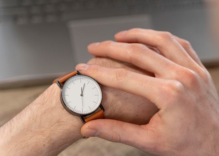 Close-up of a person checking a wristwatch near a laptop, symbolizing Dutch worker setting work hours and logging off on time. Close-up of a person checking a wristwatch near a laptop, symbolizing Dutch worker setting work hours and logging off on time.