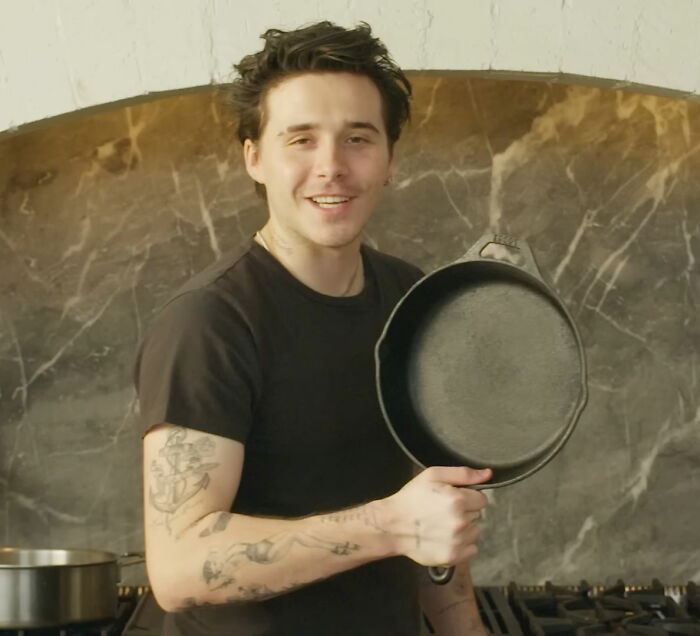 Brooklyn Beckham smiling in kitchen holding a cast iron pan, featured in self-proclaimed chef breakfast video.