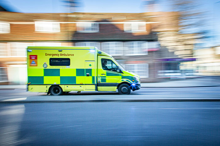 Yellow emergency ambulance speeding past houses, illustrating calling 911 urgency and efficient information.