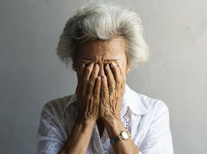 Elderly woman covering her face in distress, illustrating coworkers acting unhinged in a workplace environment.