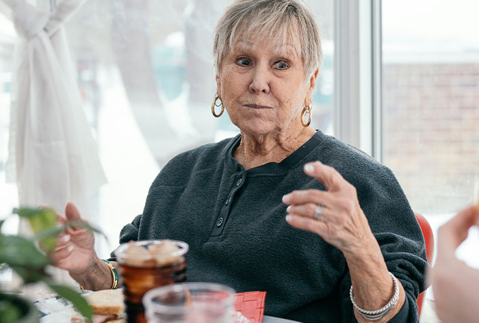 Elderly woman speaking animatedly at a family gathering, reflecting on engagement to her first cousin.