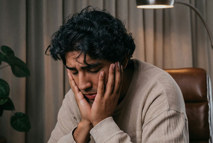 Young man with curly hair looking distressed, sitting indoors with hands on his face, reflecting on an unexpected family discovery. Young man with curly hair looking distressed, sitting indoors with hands on his face, reflecting on an unexpected family discovery.