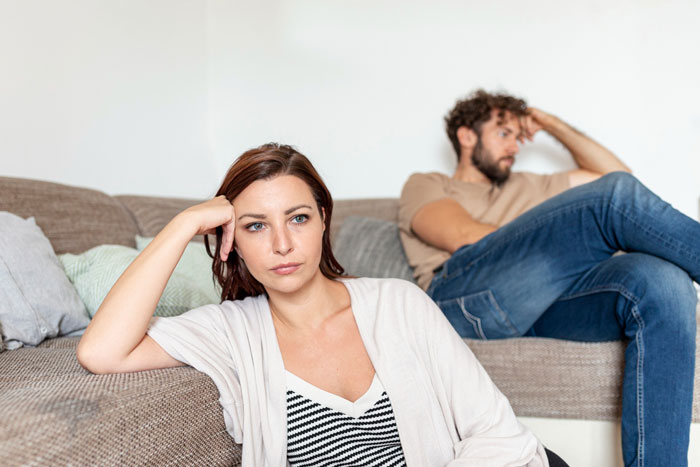 Couple sitting apart on couch looking upset, highlighting issues with prenup and infidelity clause disagreement.