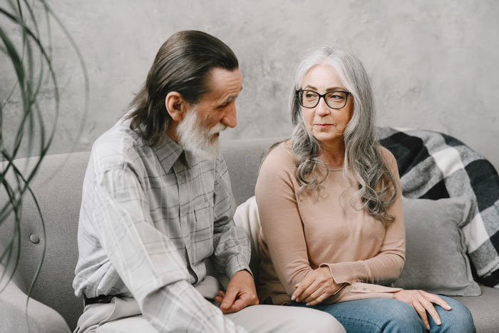 Mature couple sitting on a couch discussing prenup agreement and infidelity clause in a tense engagement conversation.