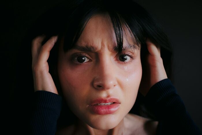 Close-up of a terrified woman with tears and hands on her head, capturing a real-life moment fitting a horror movie scene.