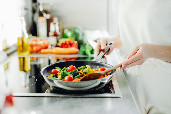 Person cooking colorful vegetables in a pan on stove, illustrating ex house drama relationship themes in a home kitchen setting.