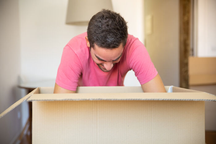 Man in a pink shirt looking into a large cardboard box, illustrating couples having petty fights during Christmas period.