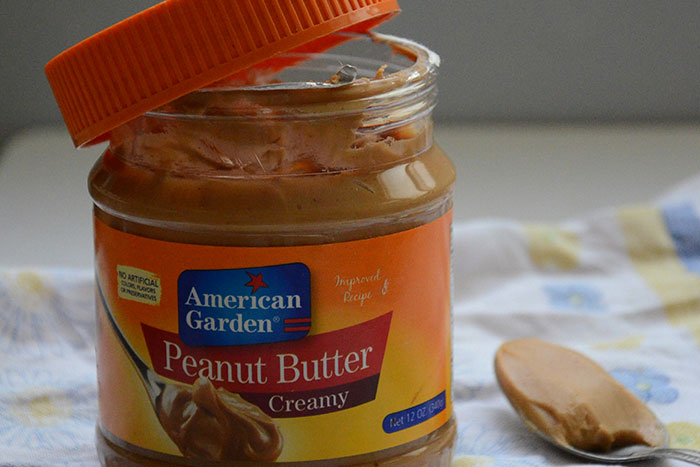 Open jar of American Garden creamy peanut butter with a spoonful of peanut butter on a tablecloth.