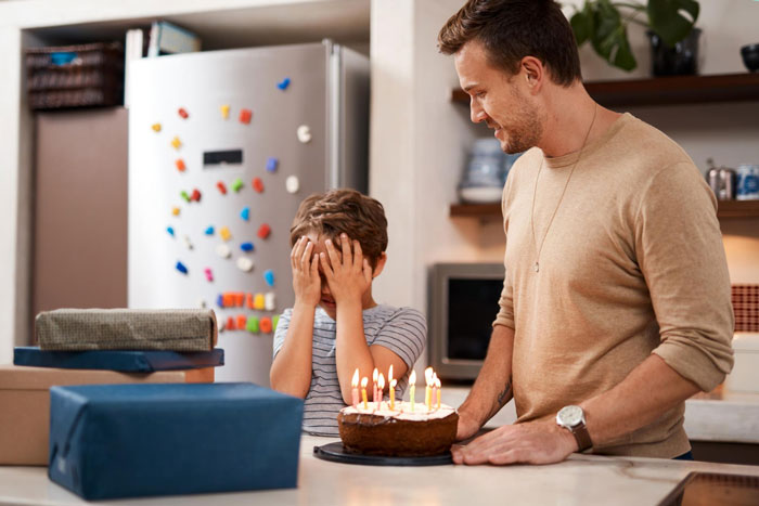 Young boy covering face while adult holds birthday cake, highlighting aunties' favoritism and kids' feelings in family celebrations.