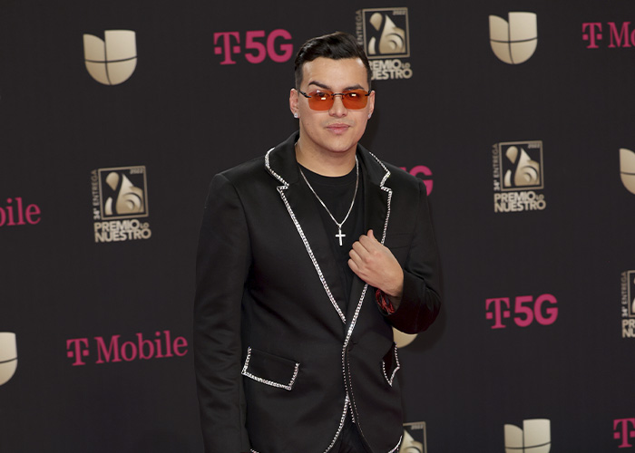 Famous singer wearing glasses and a black suit with silver trim at a red carpet event posing confidently.