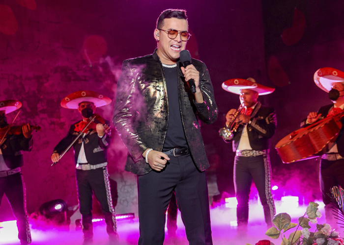 Famous singer performing on stage with mariachi band, under dramatic purple lighting and smoke effects. Famous singer performing on stage with mariachi band, under dramatic purple lighting and smoke effects.