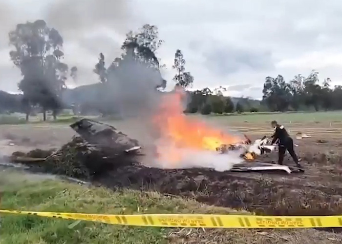 Burning plane wreckage in a field after a crash with emergency personnel nearby, related to famous singer plane crash.