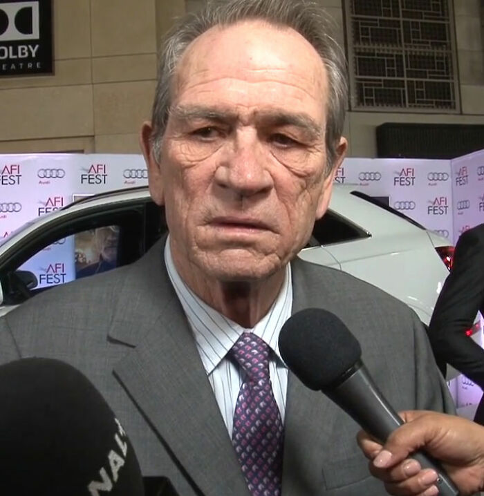 Tommy Lee Jones speaking during an interview at a red carpet event with microphones in front of him.