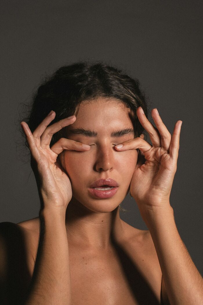 Young woman with closed eyes touching her eyelids, expressing surprise after discovering a DNA test plot twist.
