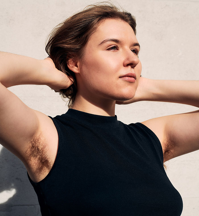 Young woman with natural body hair, embracing body positivity and women's health awareness outdoors.