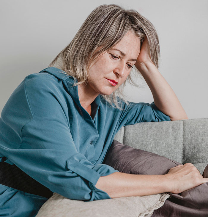Woman in a blue shirt looking thoughtful and concerned, reflecting on issues related to women’s bodies and health.