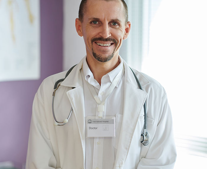 Smiling male doctor in white coat with stethoscope, representing women's health and body awareness topics.