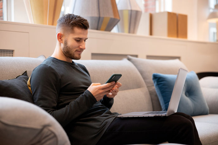 Young man sitting on a couch using phone and laptop, representing woman thinks she found a perfect match concept. Young man sitting on a couch using phone and laptop, representing woman thinks she found a perfect match concept.