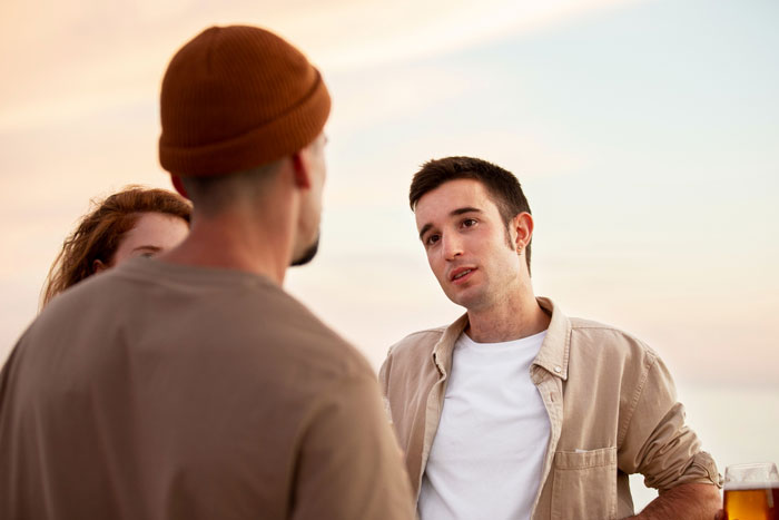 A young man discussing wedding plans and money with his friend and fiance outdoors during sunset. A young man discussing wedding plans and money with his friend and fiance outdoors during sunset.
