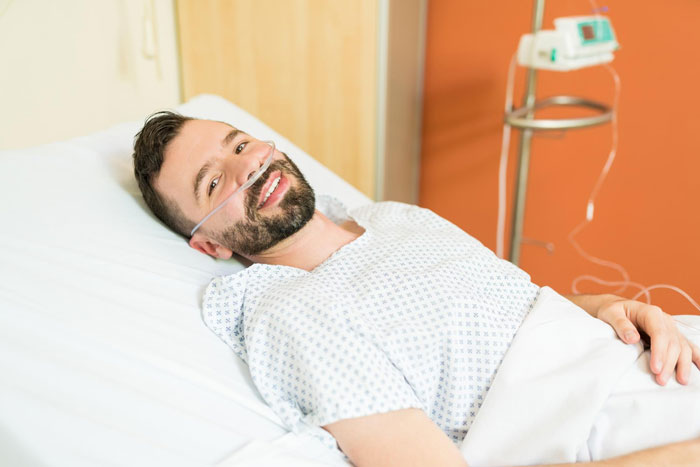 Smiling man with nasal oxygen lying in hospital bed recovering before fiance wedding with friend concerned about money issues Smiling man with nasal oxygen lying in hospital bed recovering before fiance wedding with friend concerned about money issues