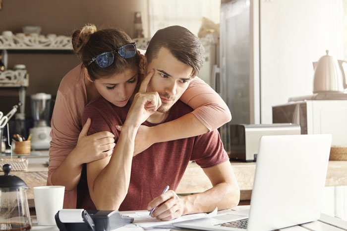 Fiance and friend discussing wedding plans and money while reviewing documents at a kitchen table with a laptop. Fiance and friend discussing wedding plans and money while reviewing documents at a kitchen table with a laptop.
