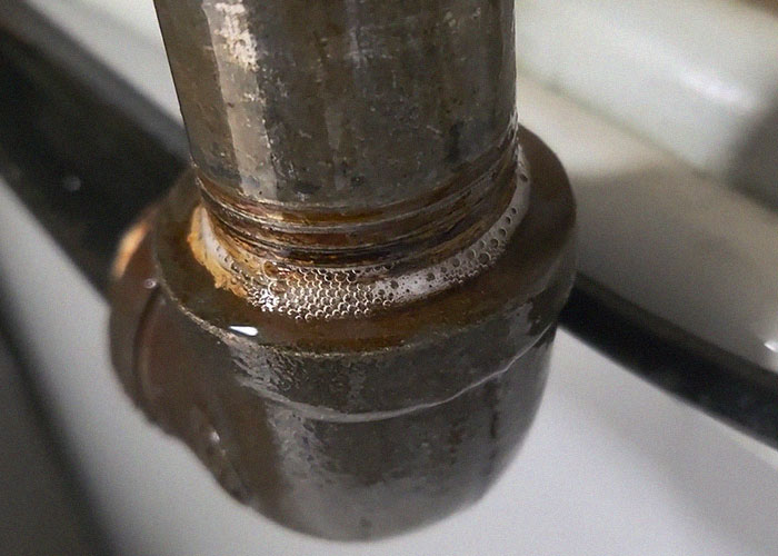 Close-up of a leaking rusty pipe joint with water bubbles, illustrating common homeownership nightmares and repair issues.