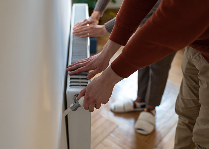 Two people adjusting a home radiator heater, illustrating common homeownership nightmares and maintenance issues.