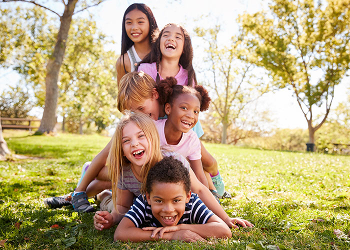 A diverse group of children happily playing outside on grass, symbolizing homeownership dreams and challenges.
