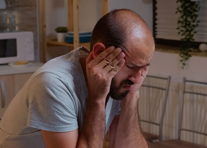 Man stressed and worried at home, experiencing common homeownership nightmares and challenges in American housing.