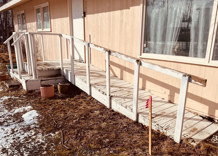 Worn and damaged wooden ramp and porch outside a house illustrating homeownership nightmares and maintenance challenges.