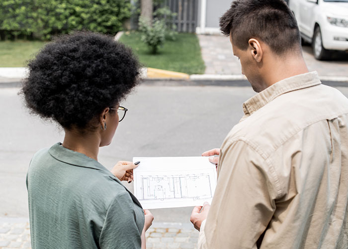 Two people reviewing a home floor plan outdoors, highlighting challenges in American homeownership dreams.