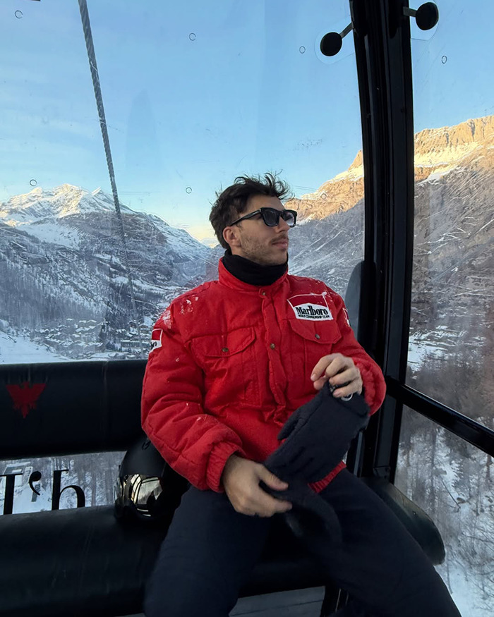 Pierre Gasly wearing sunglasses and a red jacket, sitting in a cable car with snowy mountains outside, F1 tribute context.