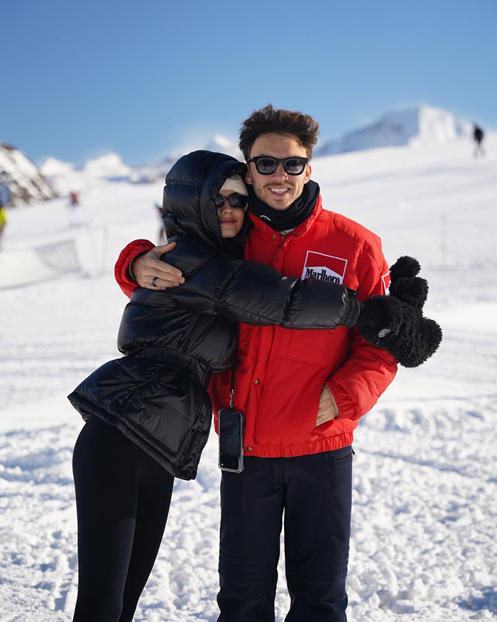 Pierre Gasly wearing sunglasses and a red jacket posing outdoors in snowy mountains during winter trip.