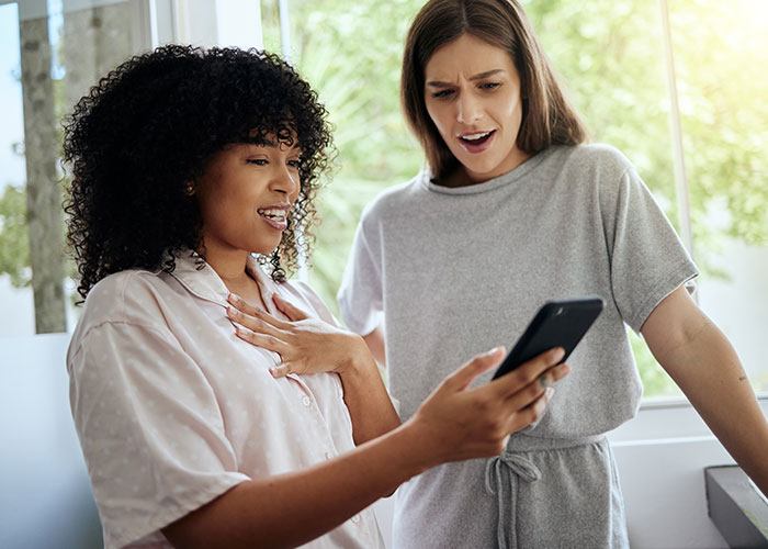 Two women looking at a phone with shocked expressions, depicting fabricated evidence of cheating and relationship drama.