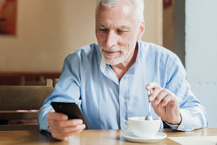 Older man upset while using smartphone at cafe, reflecting concern about tracking car with AirTag for safety.
