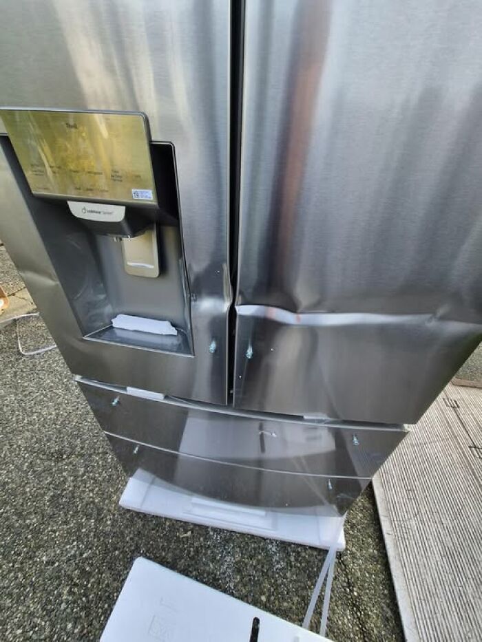Dented stainless steel refrigerator on doorstep with torn packaging, woke up expecting.