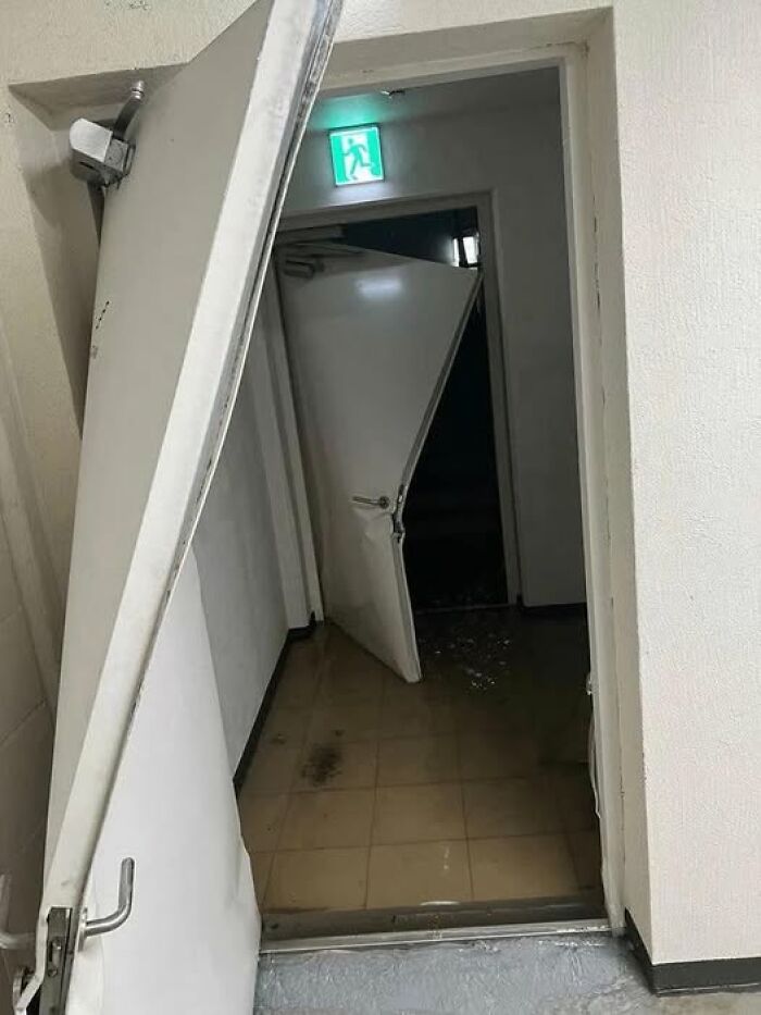 Woke up expecting a normal day, damaged doors ajar in dim stairwell with exit sign and pooled water on tiled floor