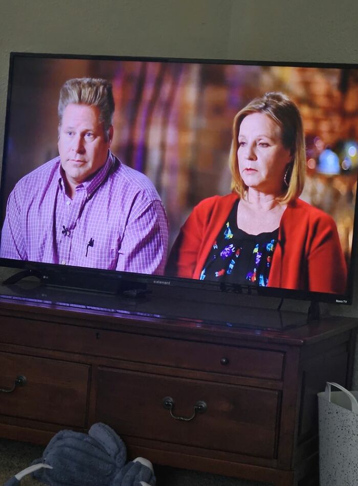 Two people sitting in an interview setting, featuring a man with a disastrous hairstyle and a woman in a red cardigan.