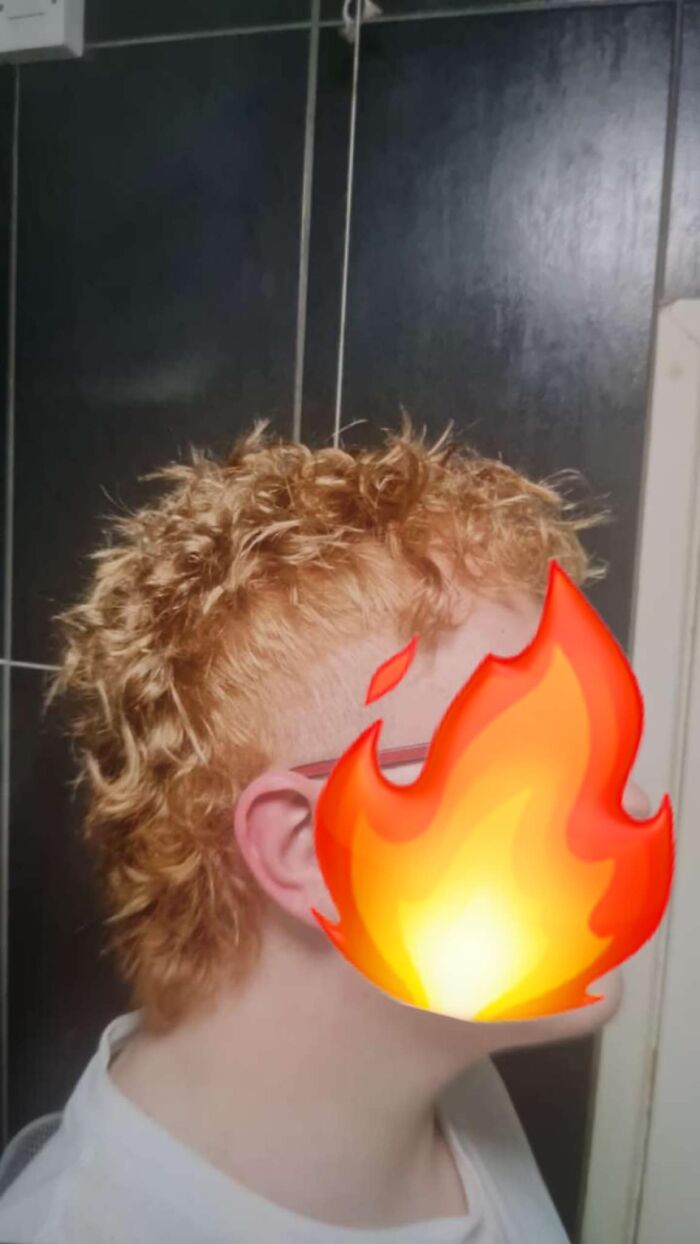 Person with curly orange mullet hairstyle and shaved sides posing indoors with a dark tiled background, showcasing disastrous hairstyles.