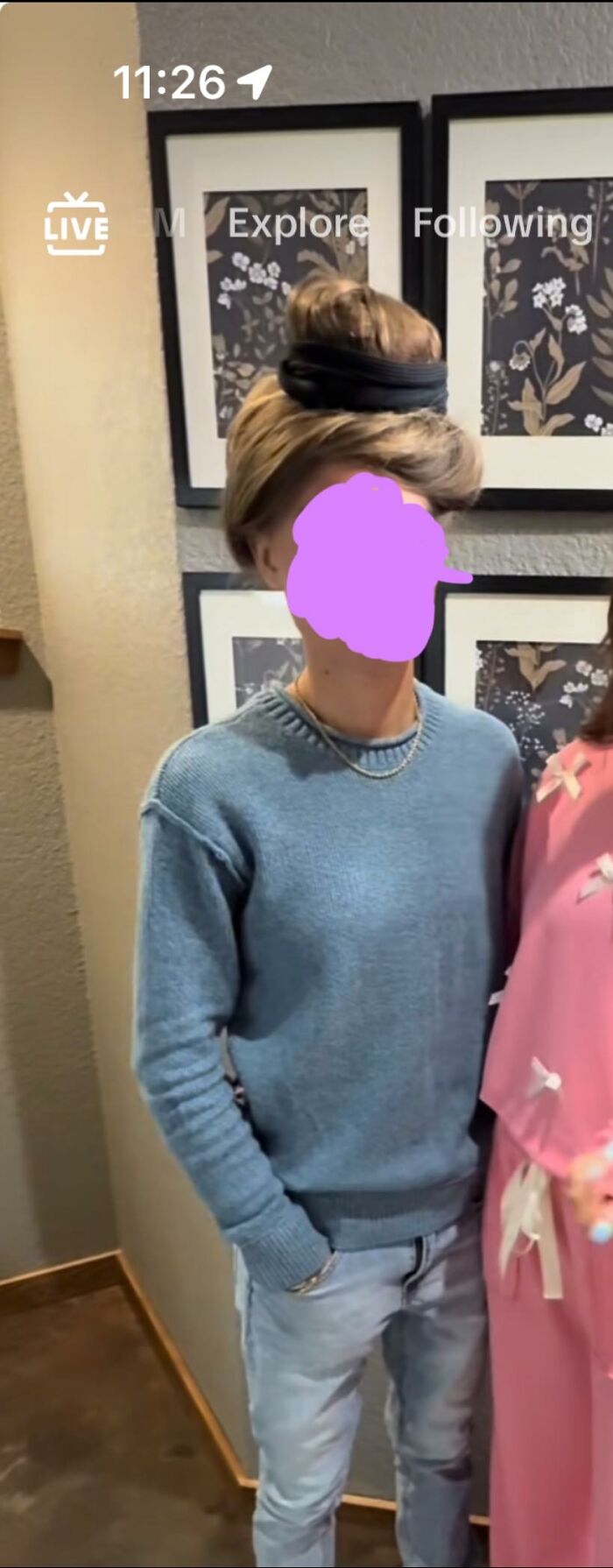 Person wearing a blue sweater with a disastrous hairstyle featuring a large hairband and messy top bun indoors.