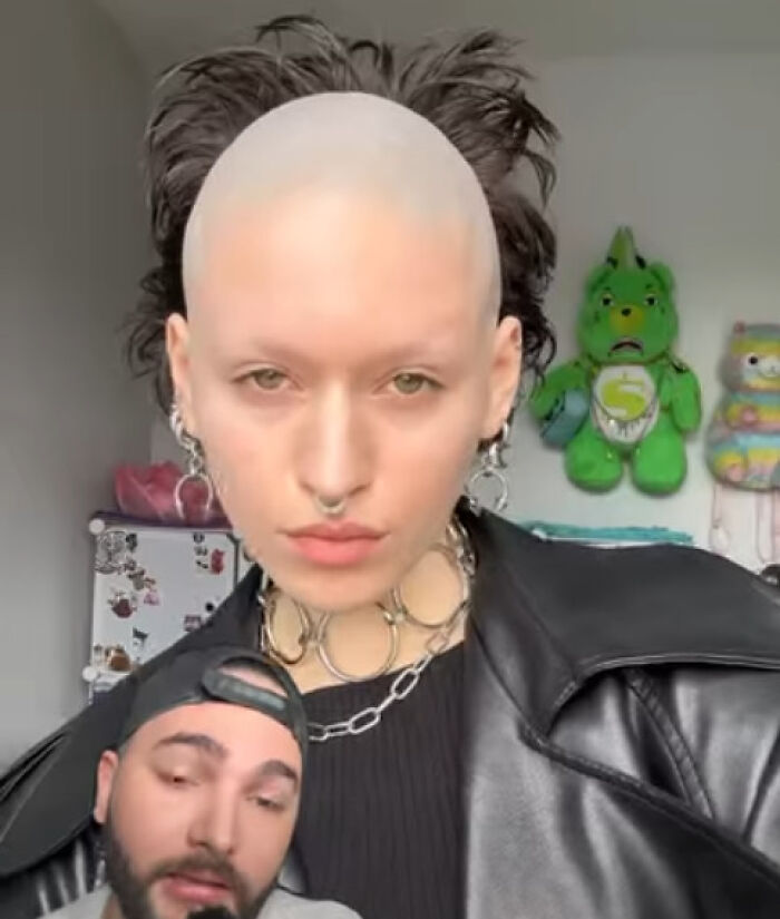 Person with a disastrous hairstyle featuring a bald front and wild hair in the back, wearing leather jacket and chains.